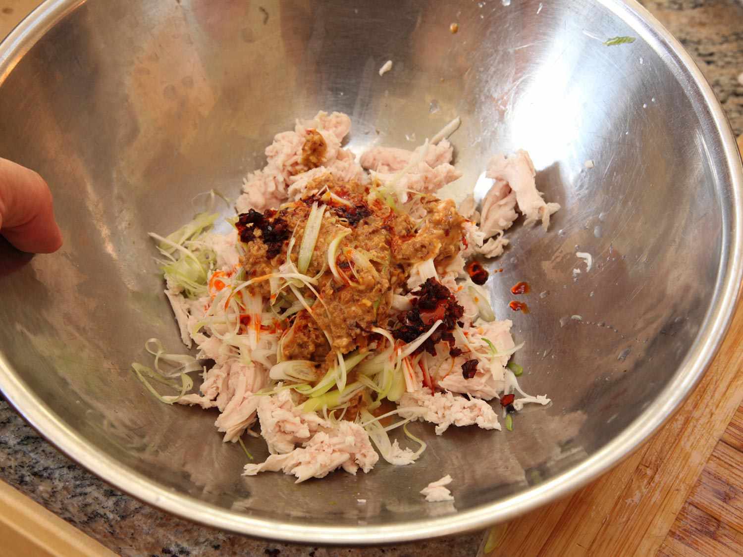 Shredded chicken breast, chile dressing, scallions, and black sesame in a metal bowl.
