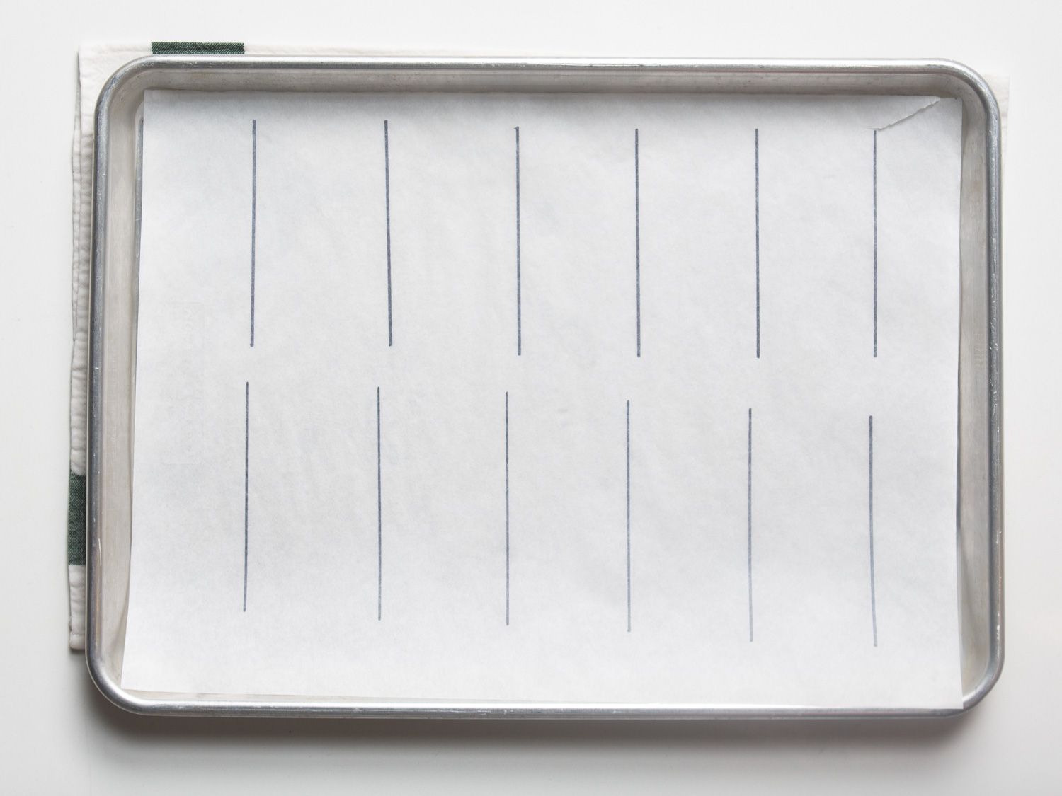 A baking sheet lined with parchment paper that has vertical lines drawn as a guide of where to pipe the éclairs.