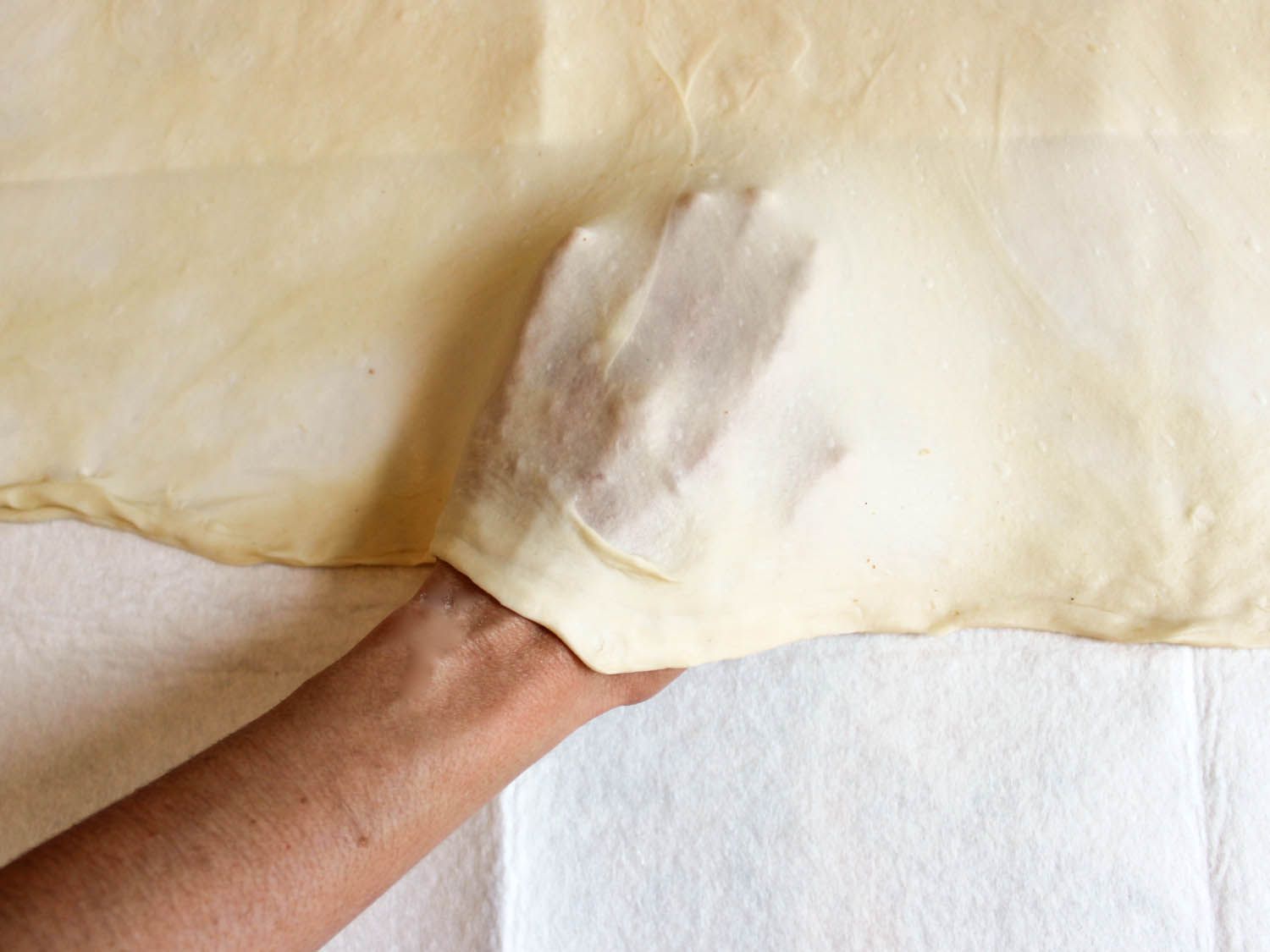 Hands are slipped under the dough so that it can be gently stretched over the cloth.