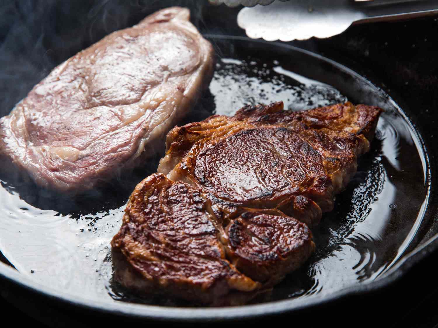 Two steaks searing in cast iron pan.