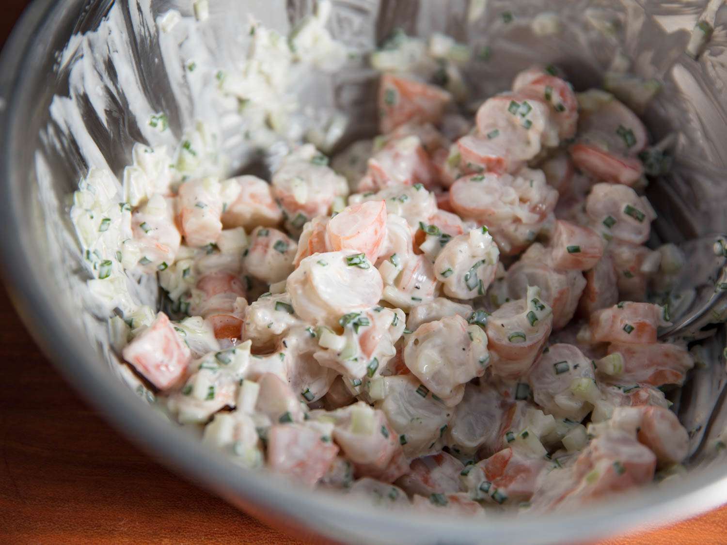 Shrimp pieces mixed with mayonnaise, chives, celery, and lemon juice in a metal mixing bowl.