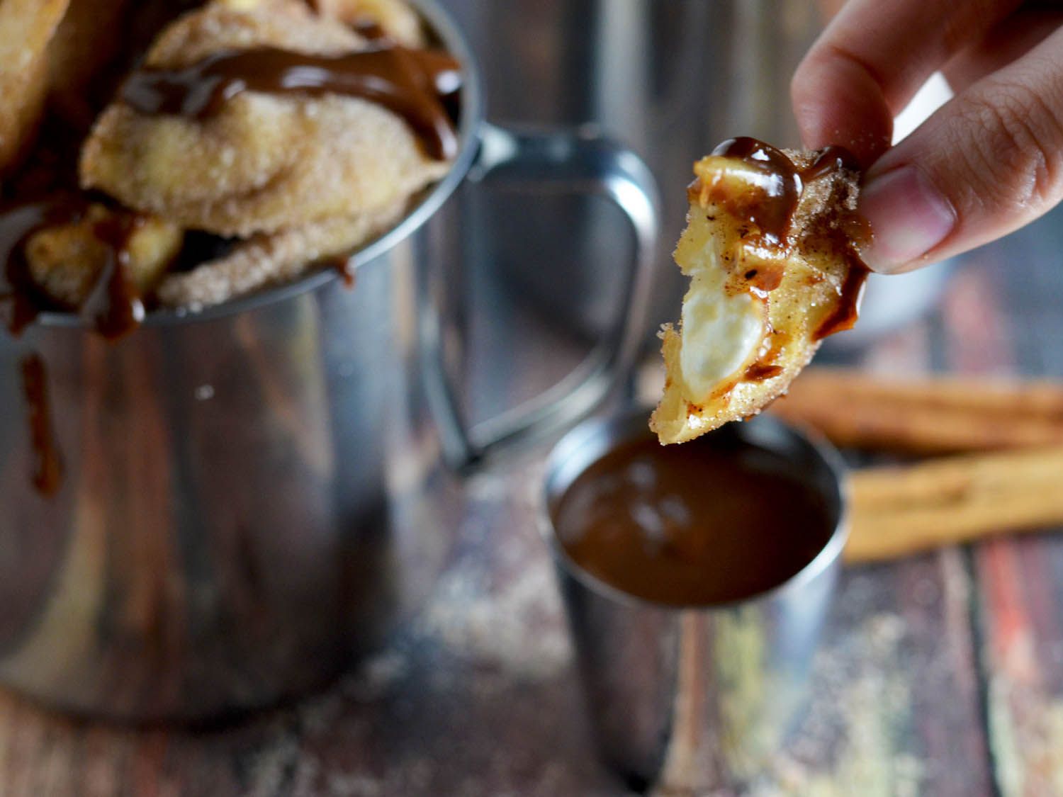A coated and dipped cream cheese wonton with a bite taken out of it is held up to the camera.