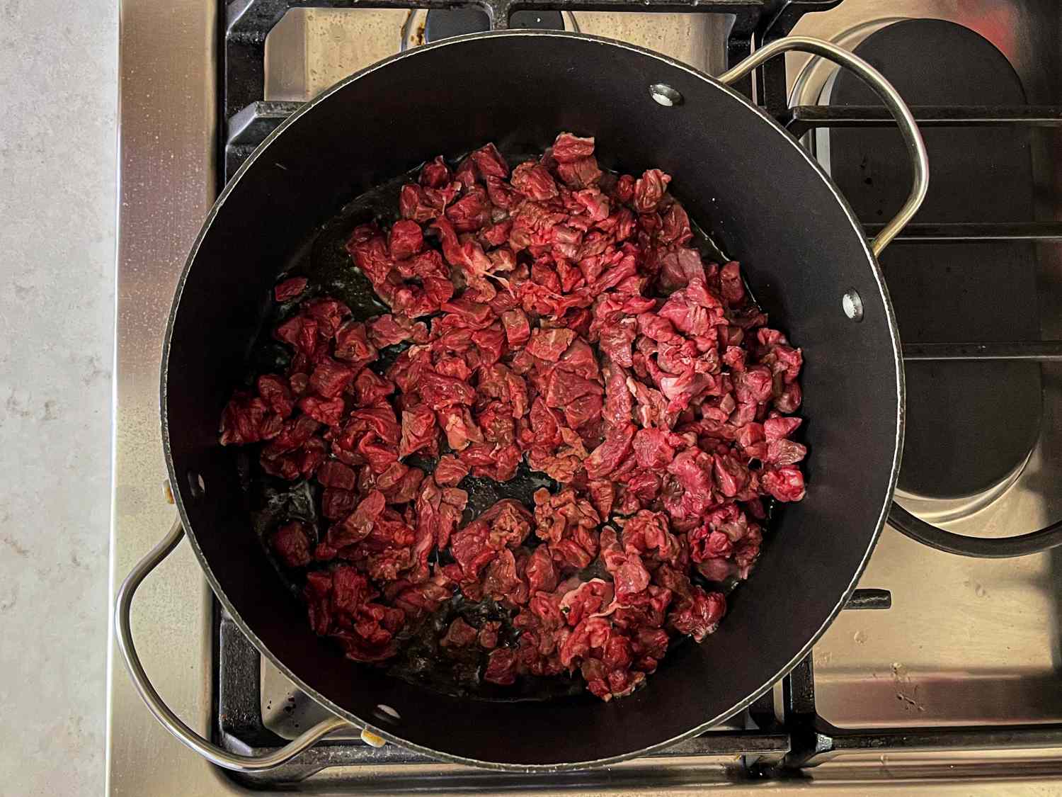 Beef and spices cooking in ghee in a large skillet.