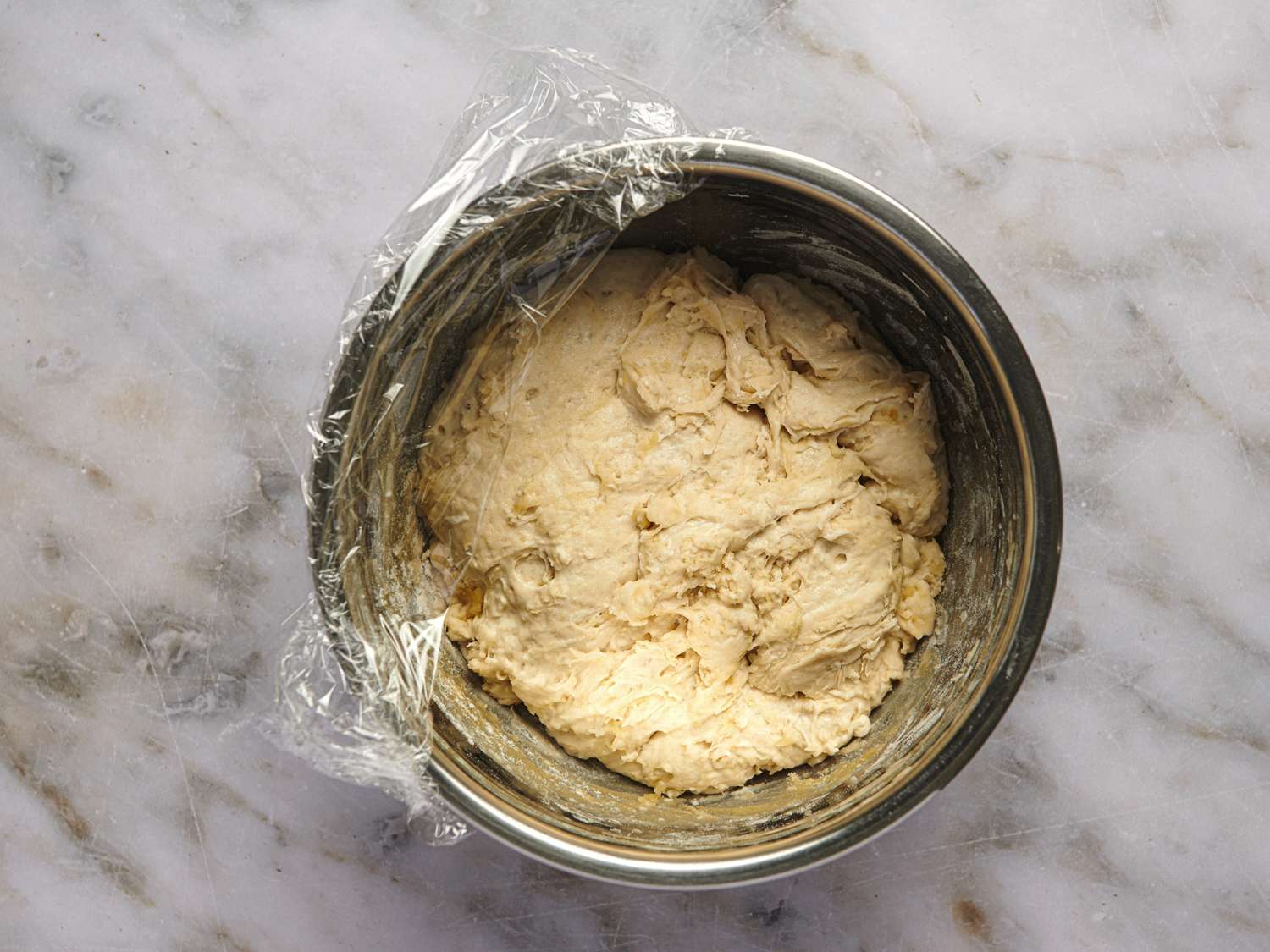 A metal bowl holding the pizza dough which has been resting at room temperature for over eight hours.