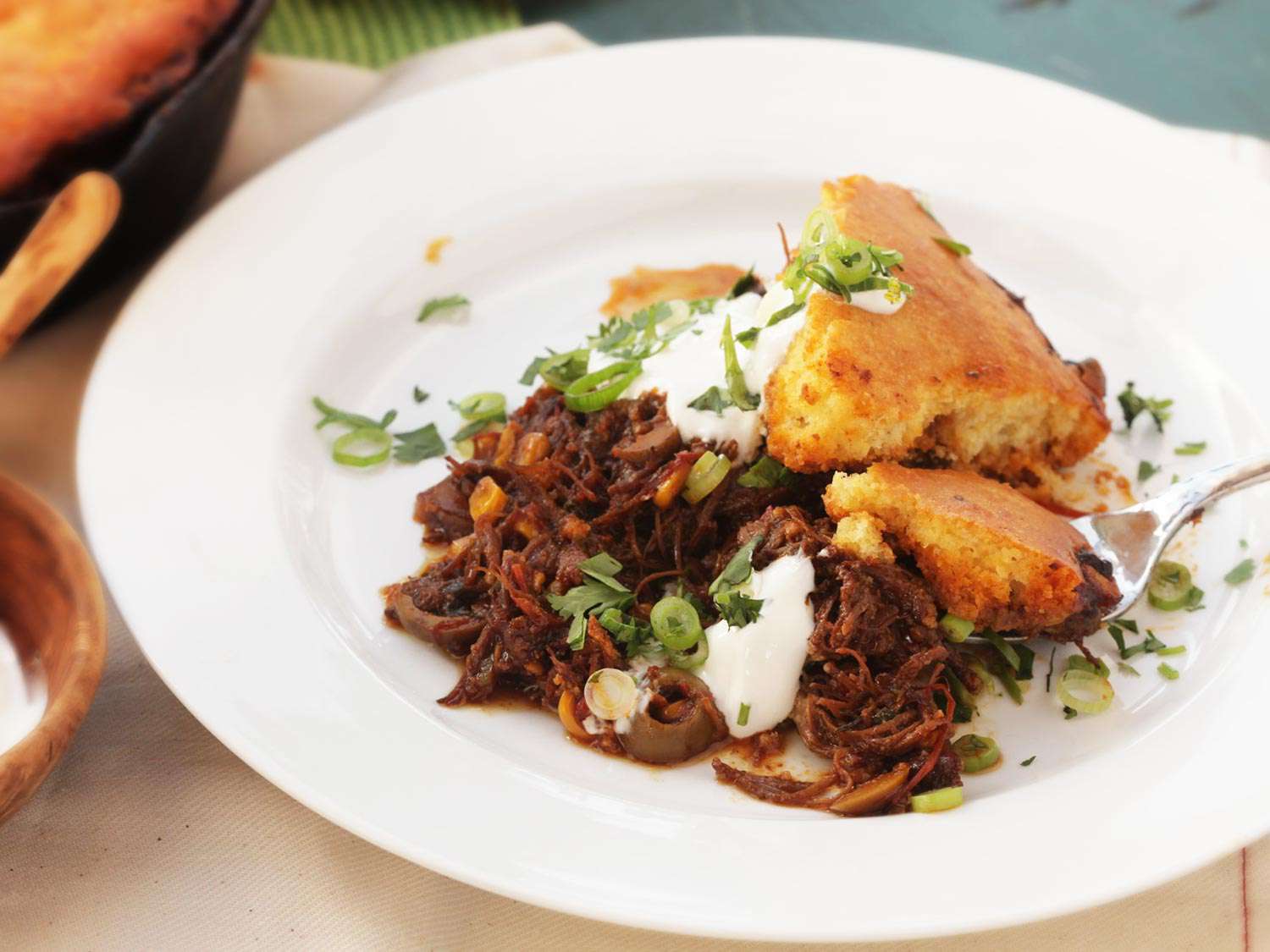 Portion of tamale pie on white plate topped with sour cream and green onions