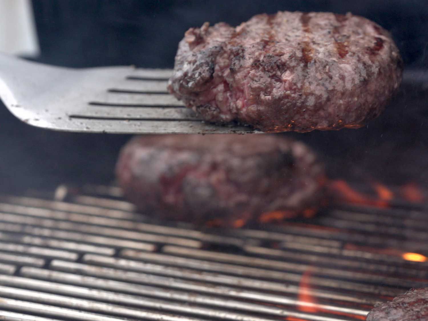 A burger being flipped on the grill with a metal spatula 