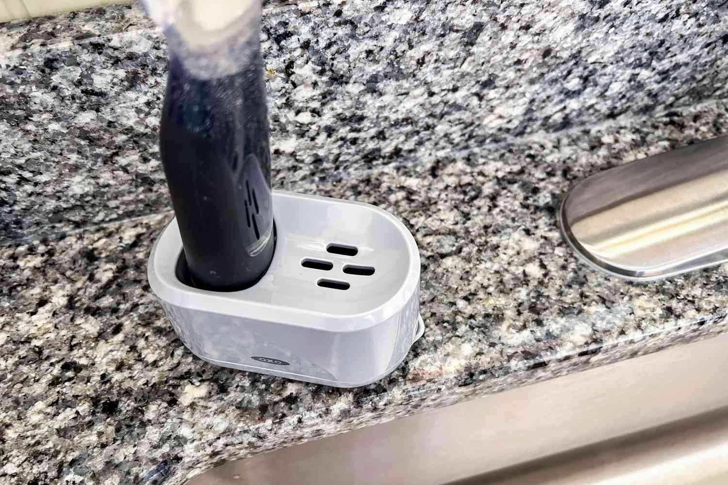 A closeup of an OXO dishwashing wand in a plastic holder next to a kitchen sink