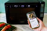 A hand holding a phone showing the Anova Precision Cooker app