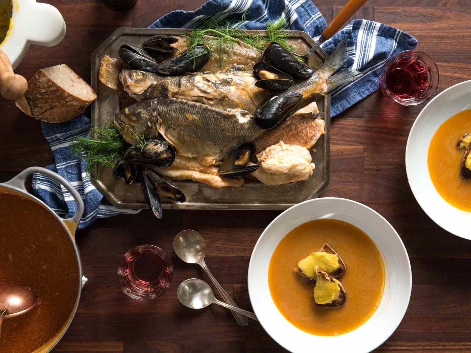 Top down view of bouillabaisse feast on the table: two bowls have been portioned and a large platter of fish fillets and mussels. 