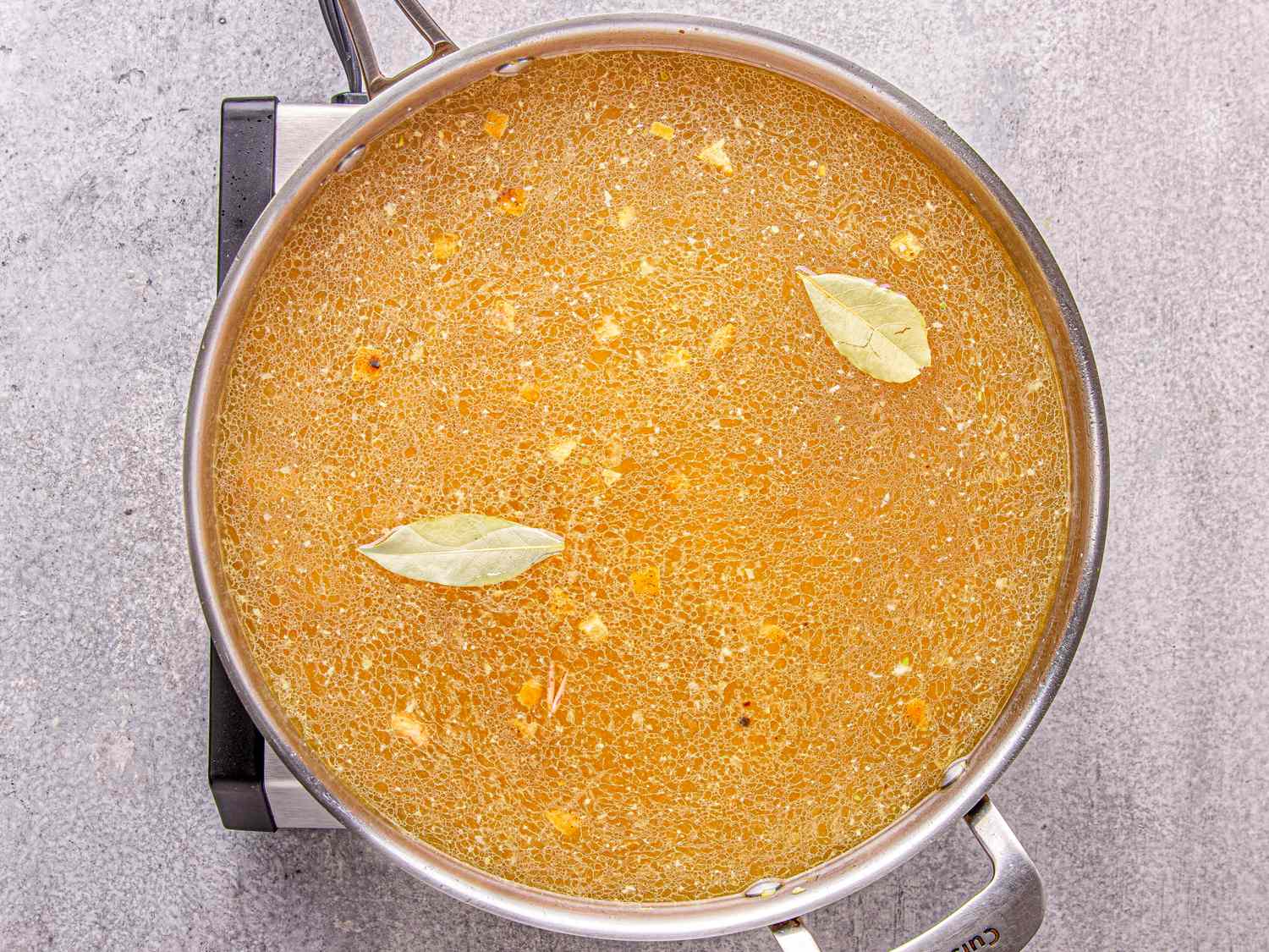 A pot containing a soup with visible ingredients like bay leaves and pieces of food