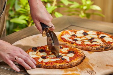 A person cutting a pie made in the Solo Stove Pi Prime Pizza Oven