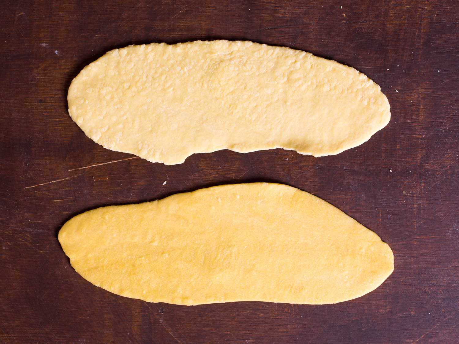 Unrested pasta dough (top) and six-hour-rested pasta dough (bottom), rolled out into slabs. The top dough is rough and jagged, while the bottom dough is smooth. 