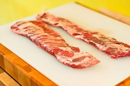Two raw skirt steaks, arranged on a cutting board.