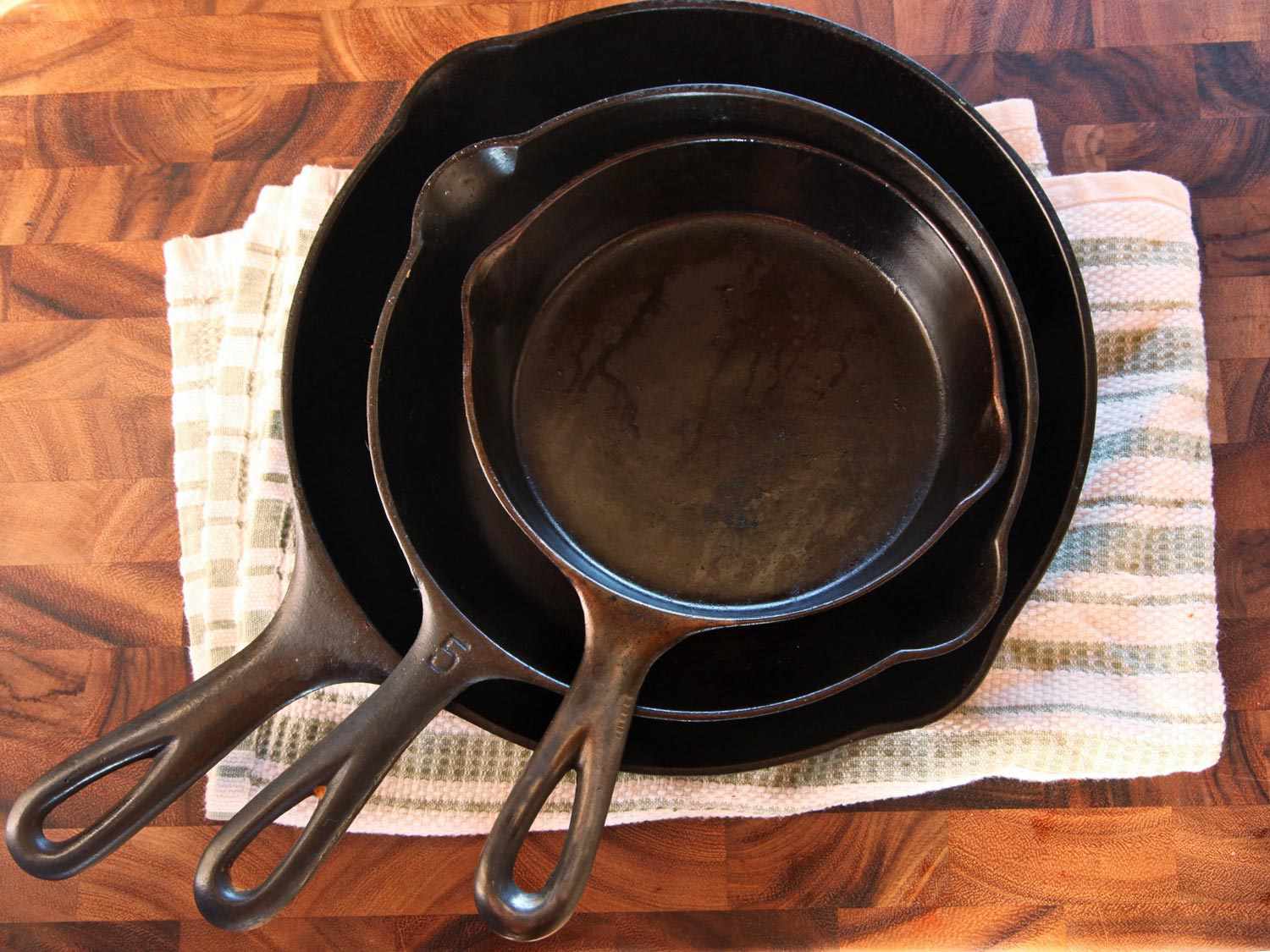 Three cast iron skillets nested on a towel that is on a wood surface