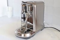 A stainless steel espresso machine with dual spouts and a milk frother