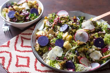 A big bowl of brassica salad with wooden serving utensils