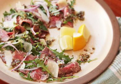 Closeup of steak carpaccio salad, served with a quartered lemon half.