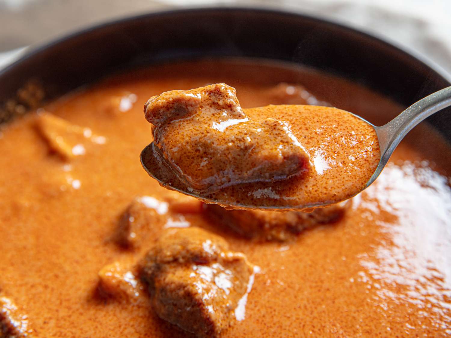 A closeup of a spoon holding a piece of meat in a creamy soup with the bowl of soup visible in the background