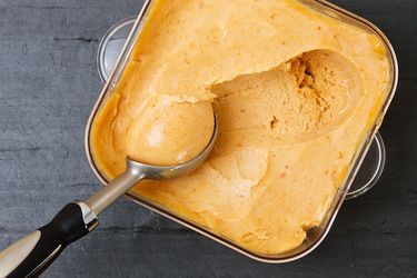 Overhead view of peach sorbet being scooped from a storage container.