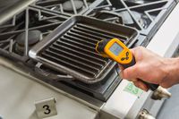 A person measuring the temperature of the Lodge 11-Inch Cast Iron Square Grill Pan