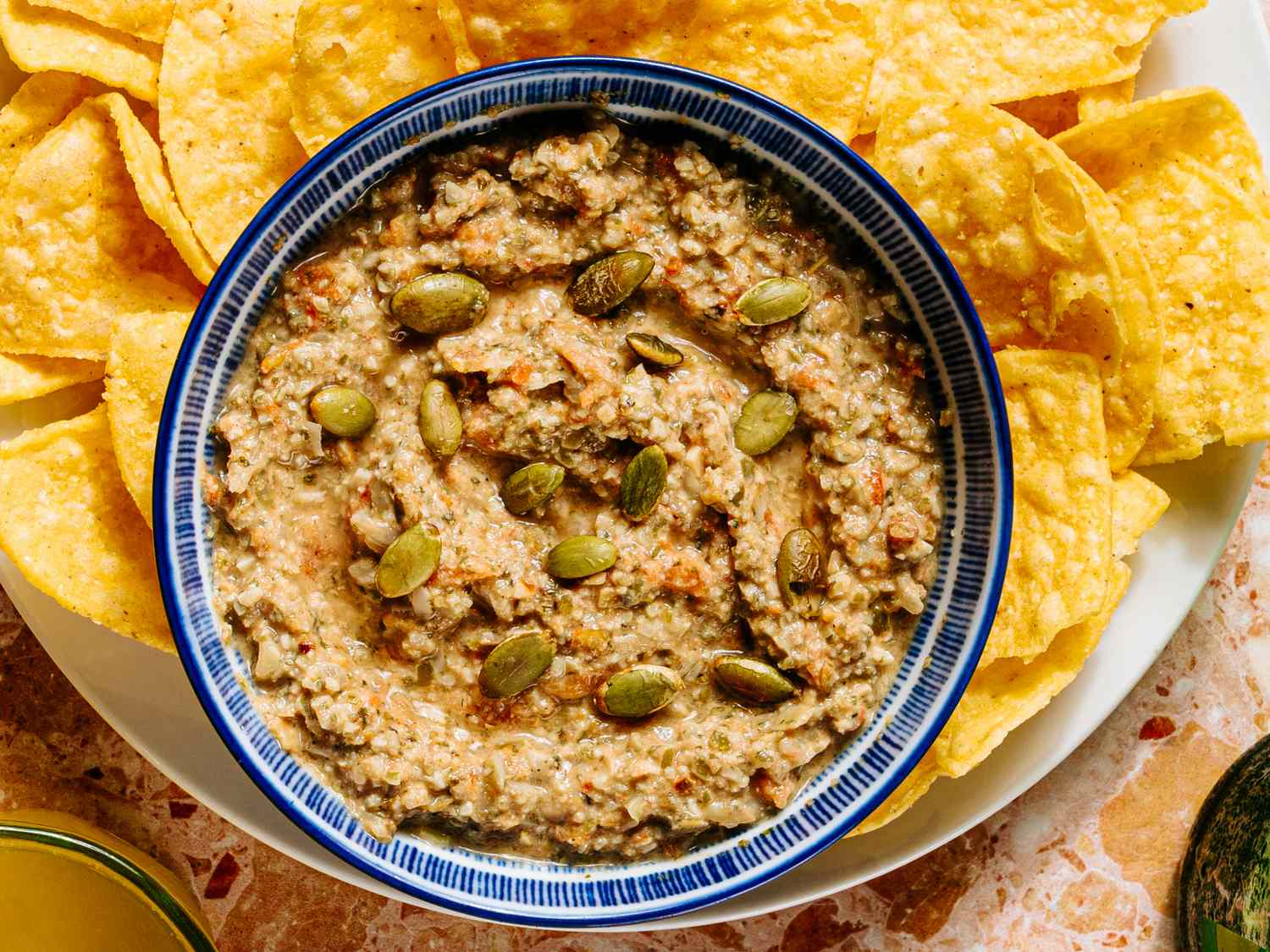 A bowl of dip garnished with seeds surrounded by tortilla chips