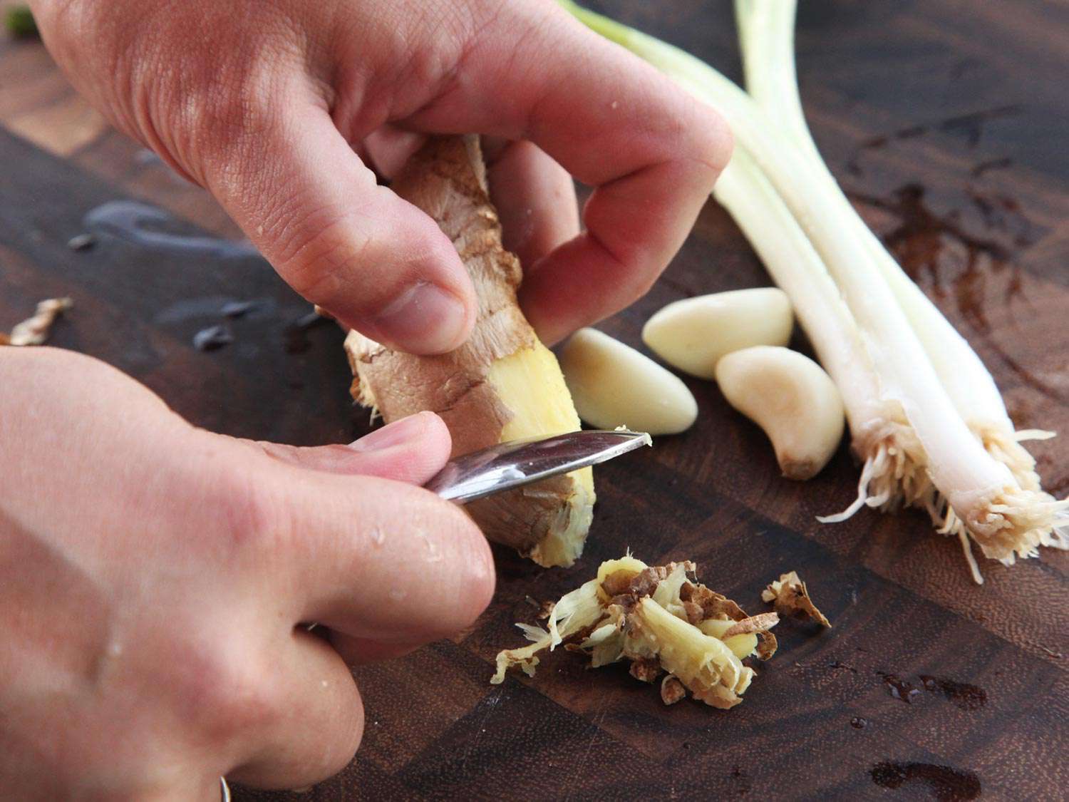 Peeling ginger root with a spoon on a wood cutting board. 