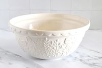 A Mason Cash bowl with embossed floral patterns on the exterior placed on a marble surface