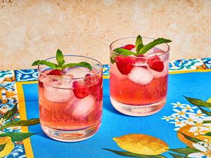 Two glasses of raspberry spritz garnished with mint leaves, placed on a colorful patterned surface