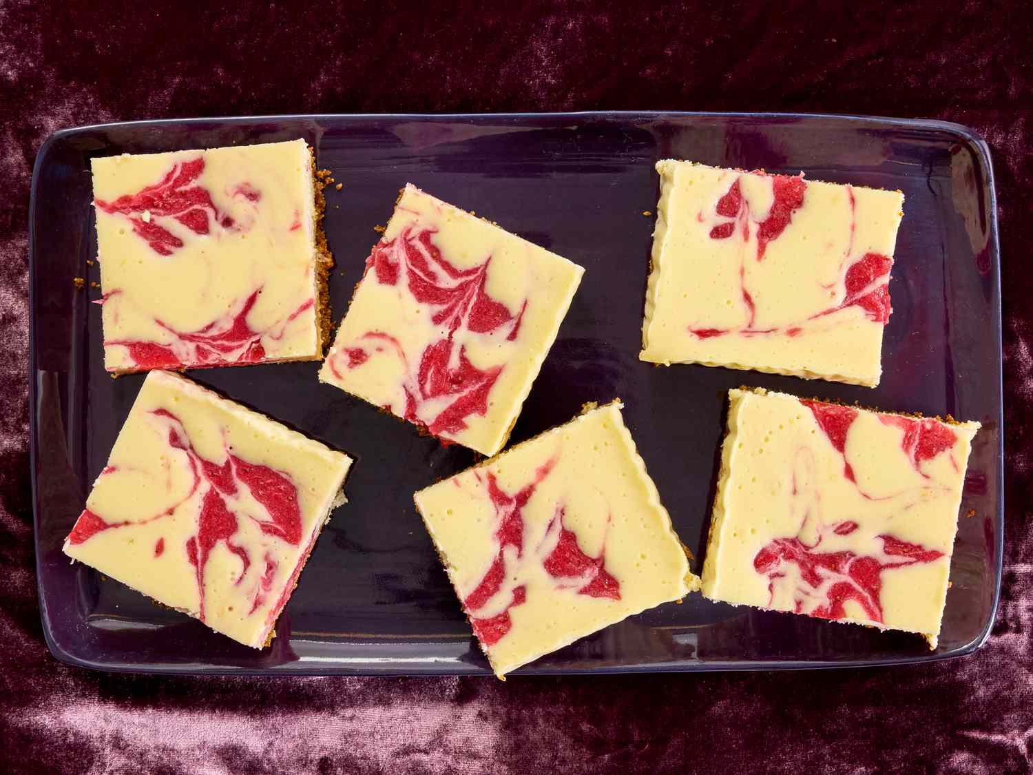 Strawberry cheesecake bars in a purple tray, on purple velvet 