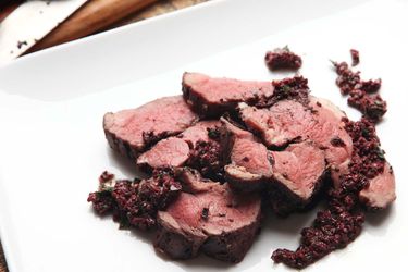 Closeup of sliced sous vide leg of lamb with black olives served on a white plate.
