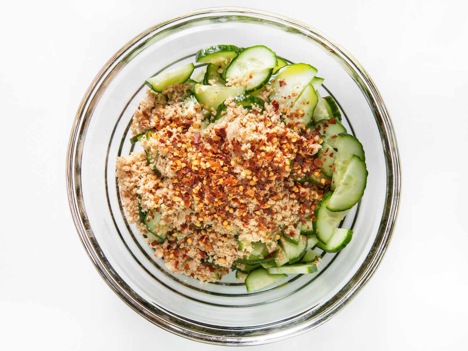 Overhead shot of plated cucumber salad with mustard oil dressing topped with crushed hazelnuts.