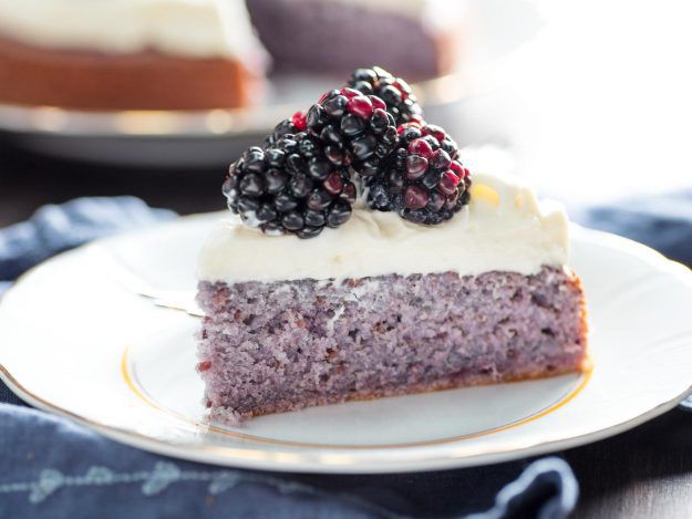 A slice of purplish blackberry cake on a plate, topped with cream cheese frosting and fresh whole blackberries
