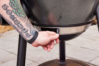 A person opens a valve on the Char-Griller E16620 Akorn Kamado Charcoal Grill