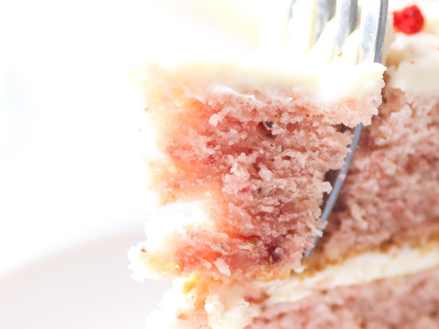 Close-up of a fork spearing a piece of strawberry layer cake.