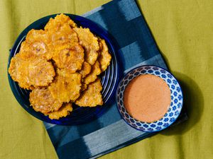 Overhead view of tostones on a blue plate with a blue napkin and bowl of dipping sauce