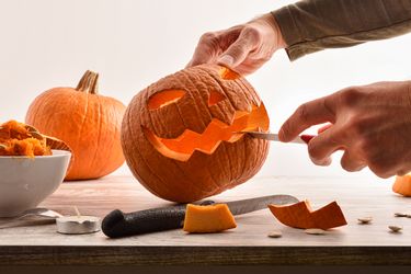 A person carving a jackolantern face on a pumpkin using a knife
