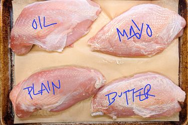 Four raw turkey breasts labeled oil mayo plain and butter on a baking sheet lined with parchment paper