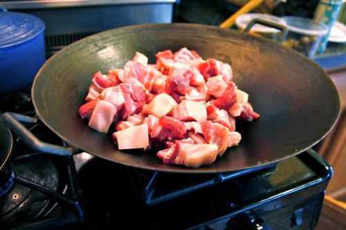 Cuts of pork belly cooking in a wok.