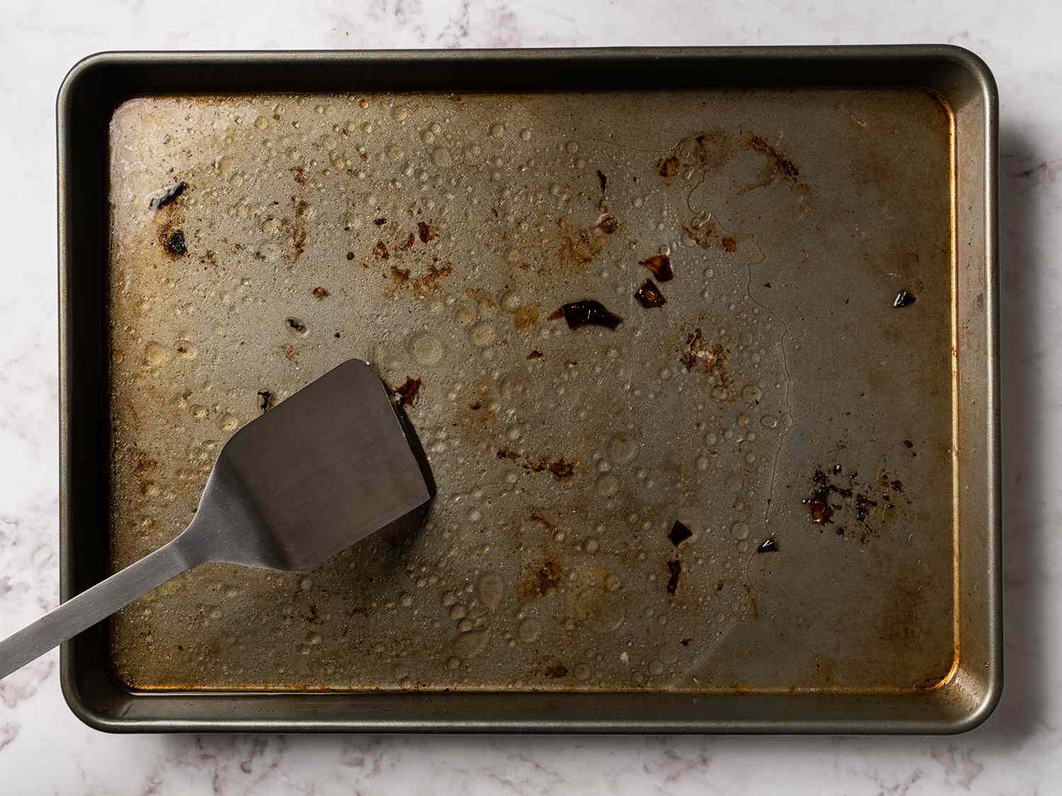 A spatula scraping off bits from the baking sheet