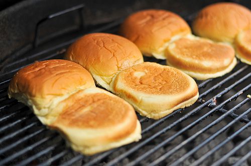 Hamburger buns lined up and open, inside down, on a grill to warm and grill the interior.
