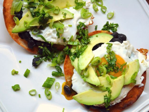 Two Black bean, avocado, and egg tostadas with avocado slices, sliced green onions, and chopped cilantro. 