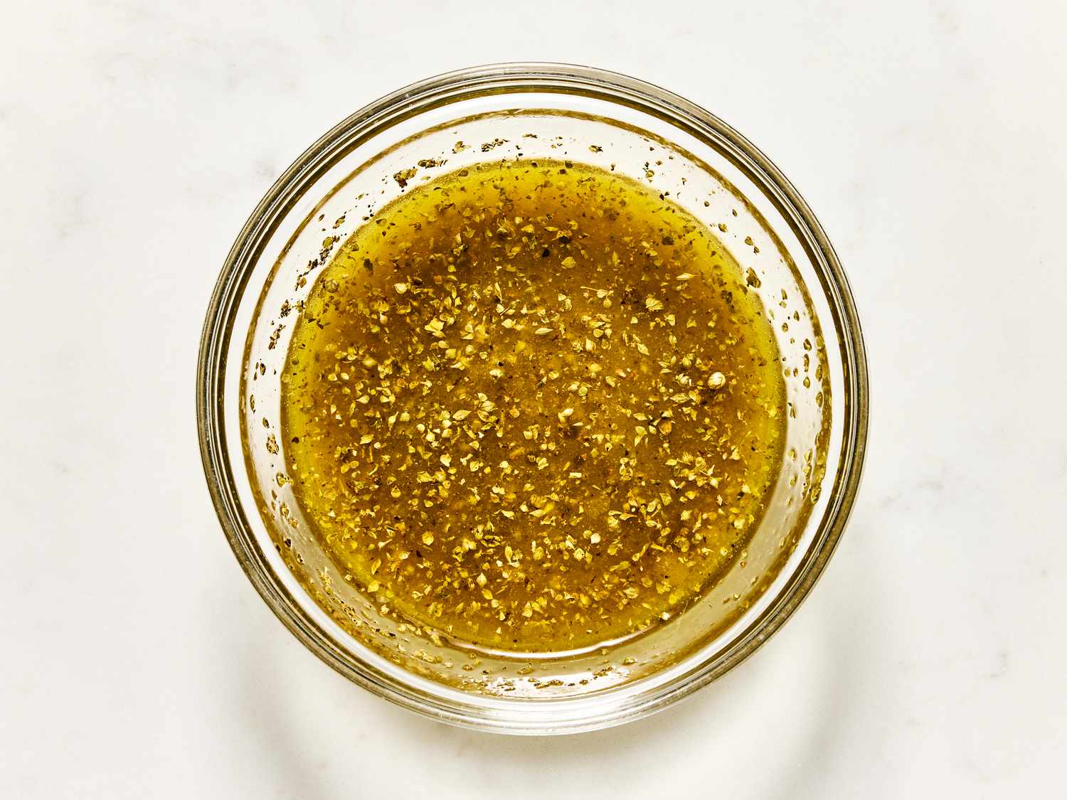 A glass bowl filled with a seasoned vinaigrette dressing, viewed from above