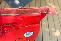 The top of a red Royal Oak All Natural Hardwood Lump Charcoal bag with a stitched seam and a warning label about carbon monoxide hazard placed on a wooden surface