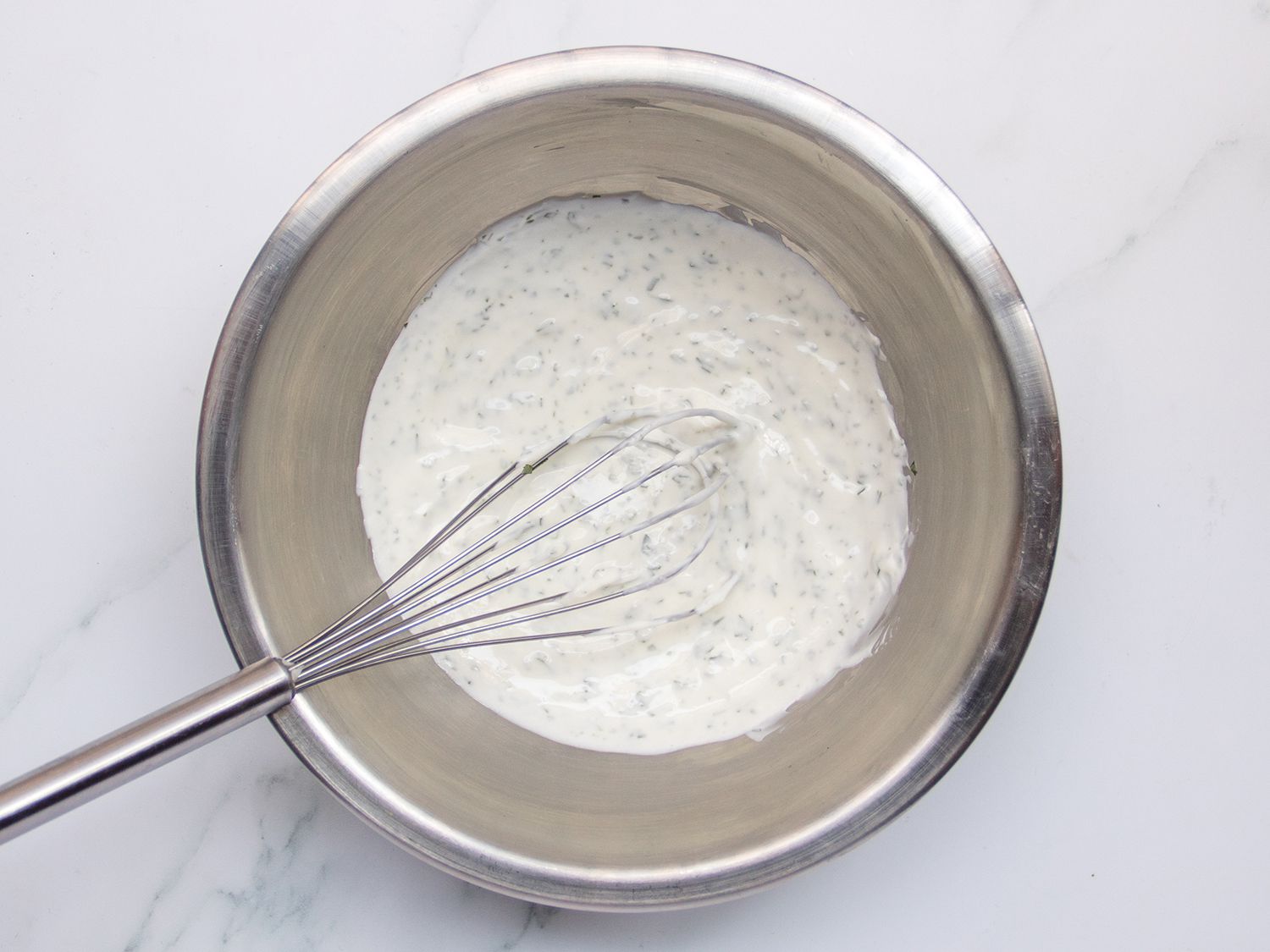 Yogurt sauce and a whisk in a silver bowl.