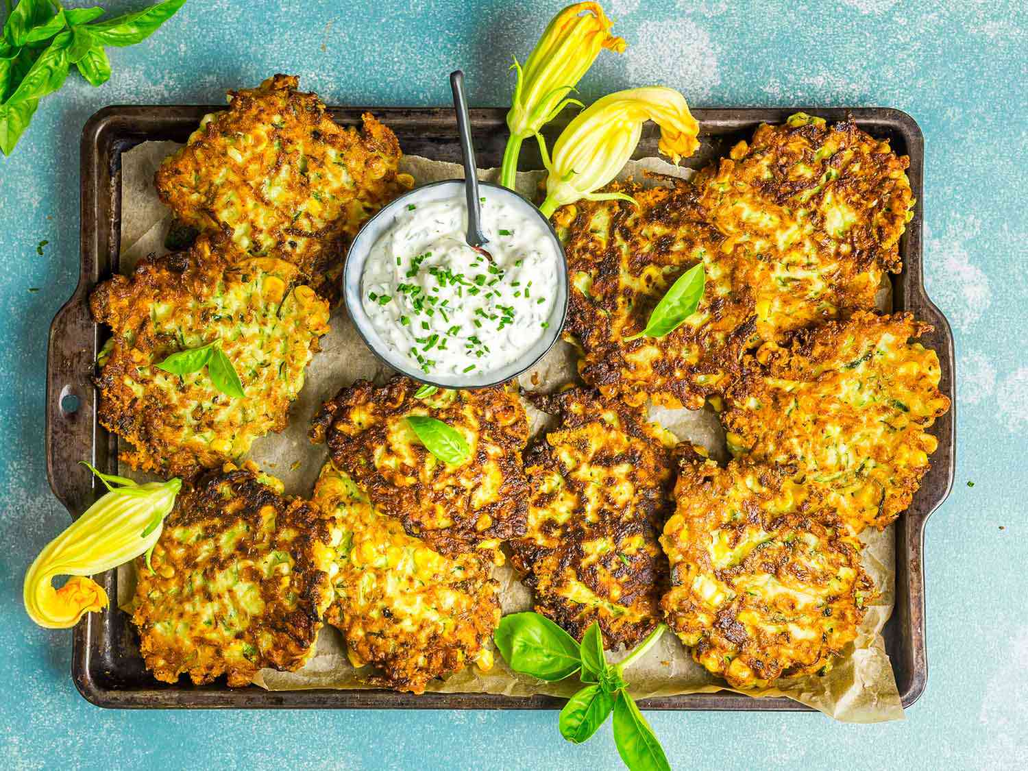 A tray of zucchini and corn fritters with a bowl of herbed sour cream