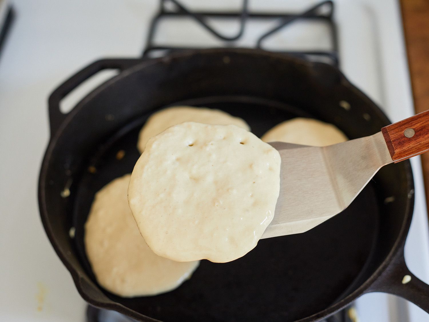 using a turner to lift a pancake from a cast iron pan