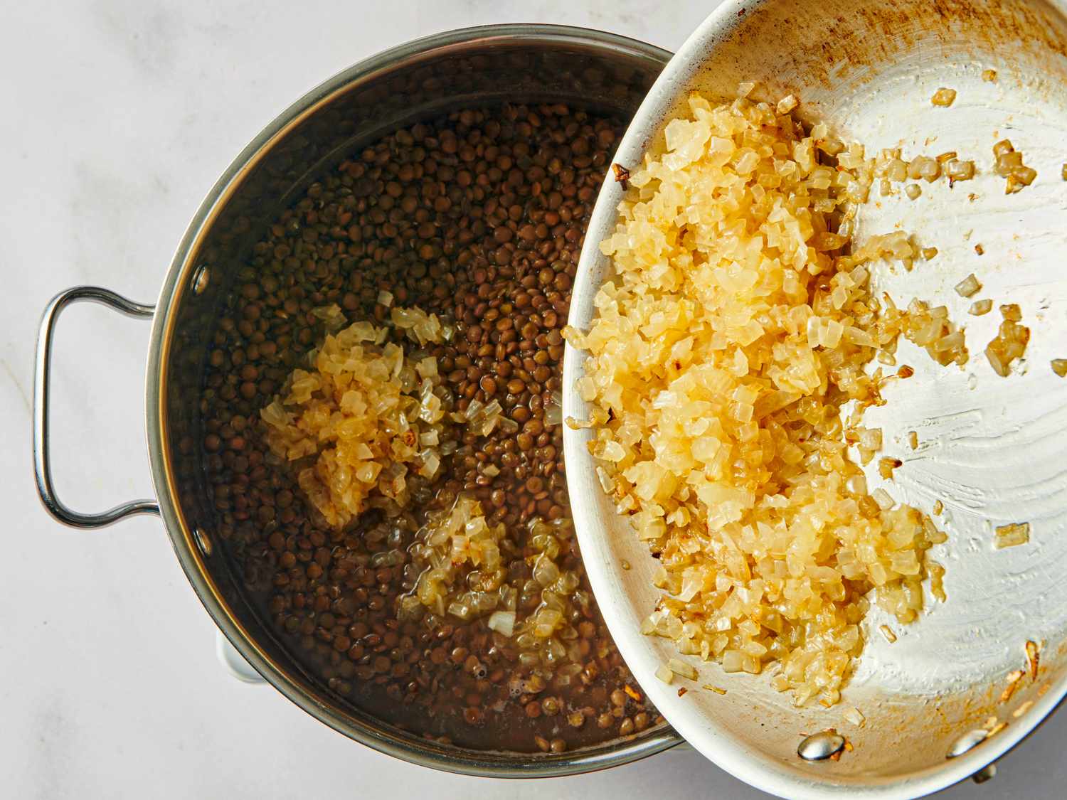 A pan of cooked lentils with caramelized onions being added from a separate dish
