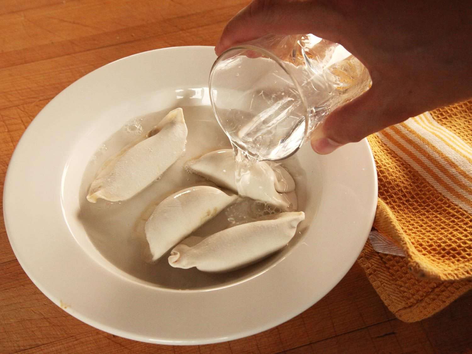Pouring water into a bowl of frozen dumplings.
