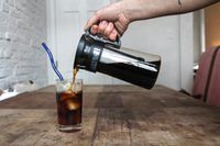 A person pouring cold brew from a carafe into a glass.