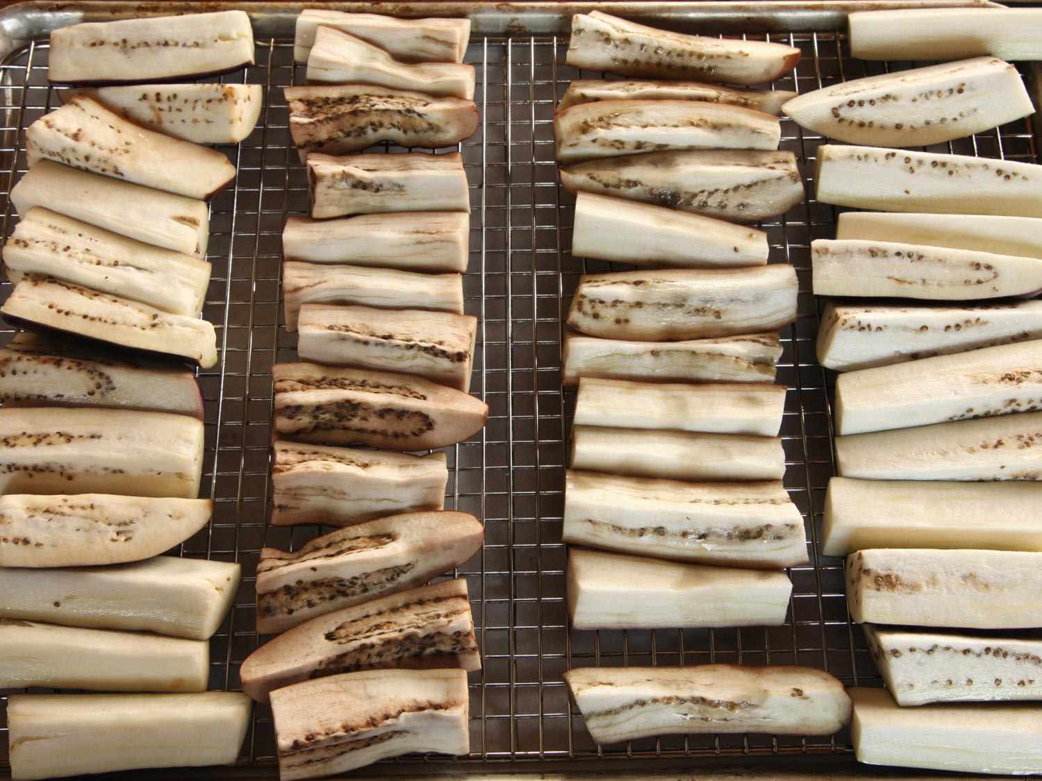 Chinese eggplant has been quartered lengthwise, cut into 4-inch segments, and arranged in rows on a drying rack.